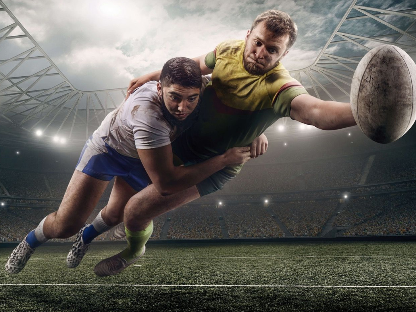 Rugby player diving forward with ball in stadium